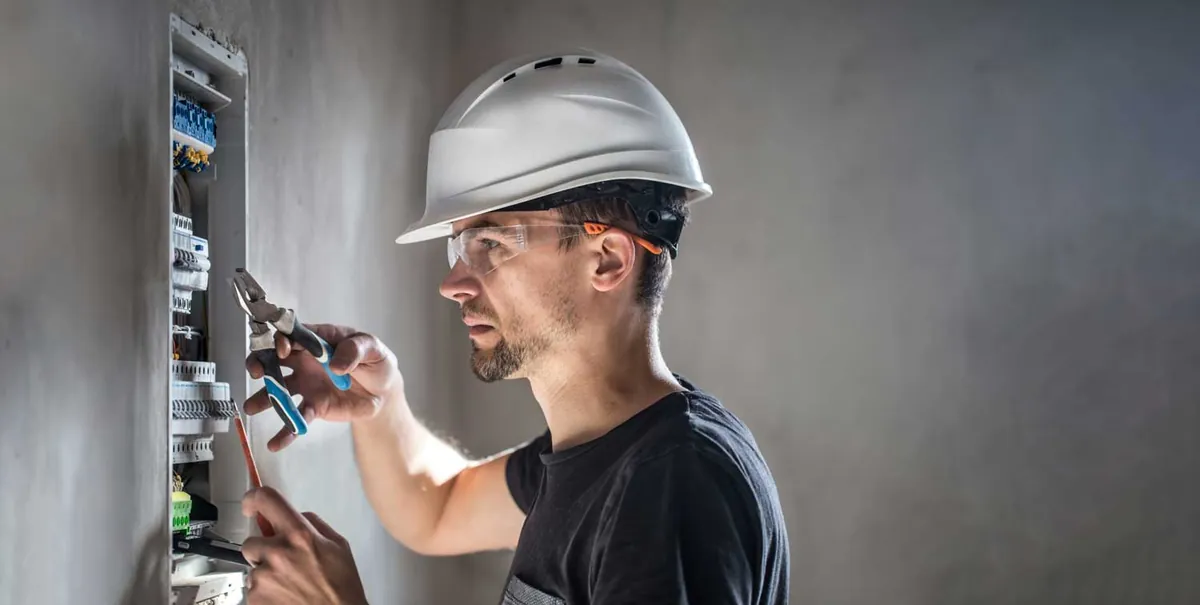 Electrician in a hard hat and safety glasses working on a distribution panel