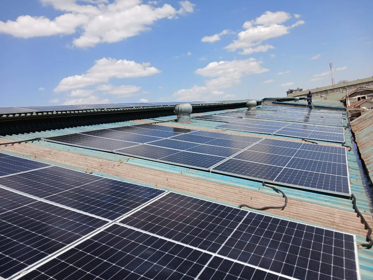 Technician cleaning solar PV panels on a factory roof with turbine ventilators